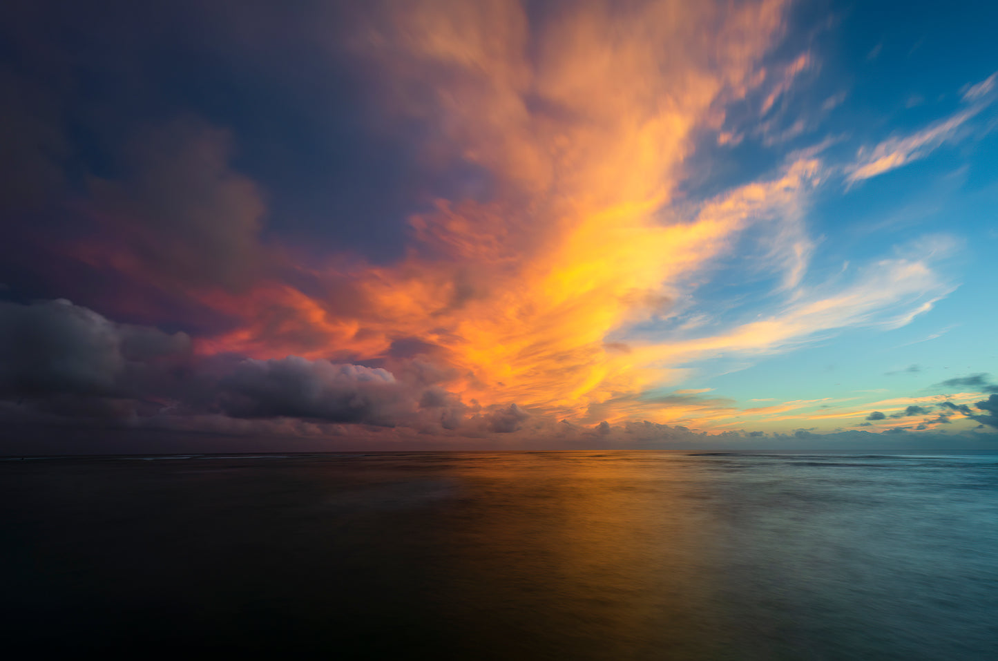 A vibrant sunset with pink, yellow and orange colored clouds over a calm ocean in Oahu Hawaii.