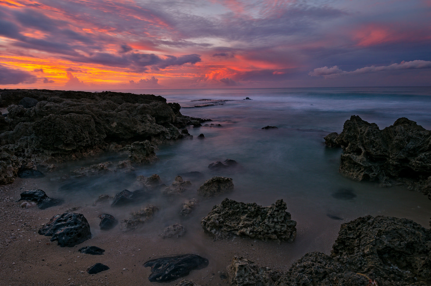 A beautiful sunset over a lava rock tidal pool and a calm ocean captured on the North Shore of Oahu.