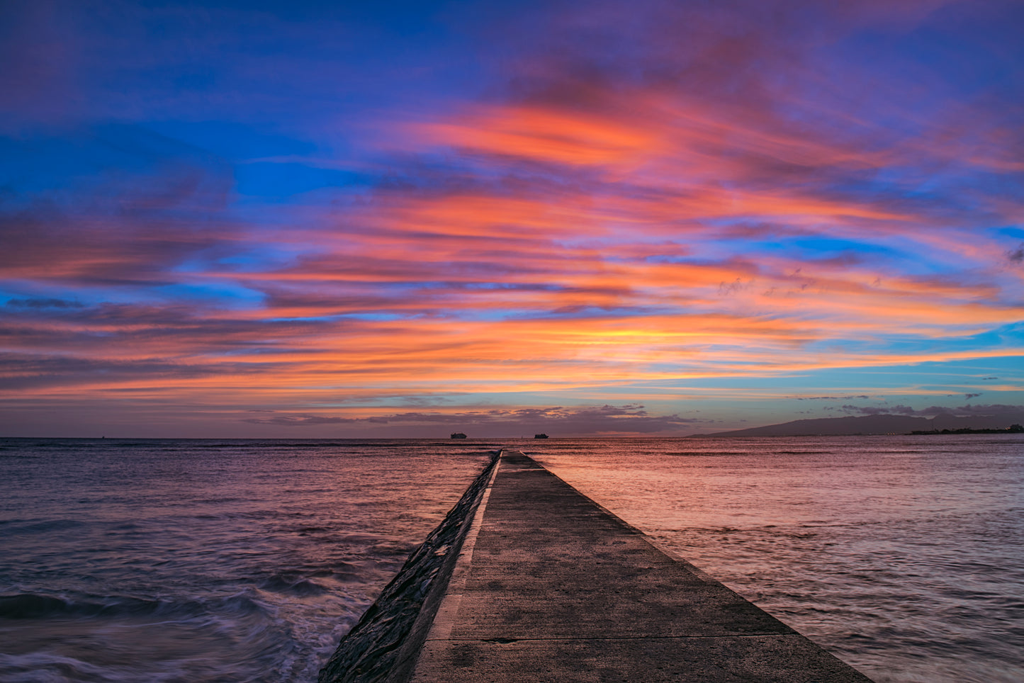 The pier at Queen's Beach in Waikiki Hawaii during a beautiful sunset with red, orange, yellow and blue color in the sky.