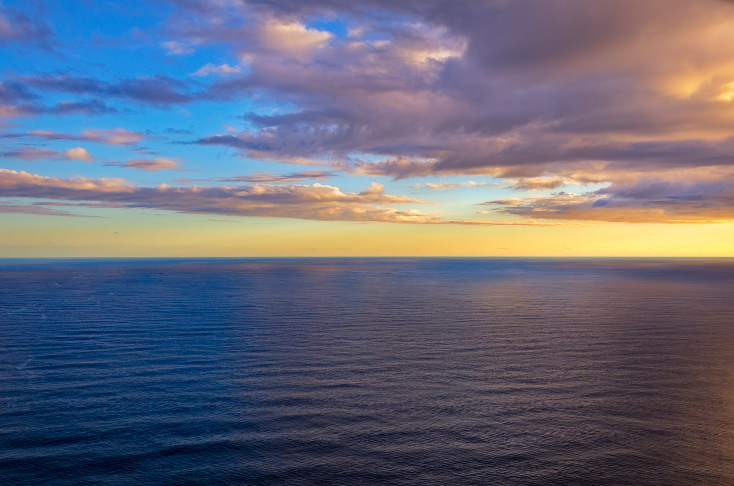 A tranquil view of the Pacific Ocean between Oahu and Kauai (Hawaii) at sunset with a cloudy sky.